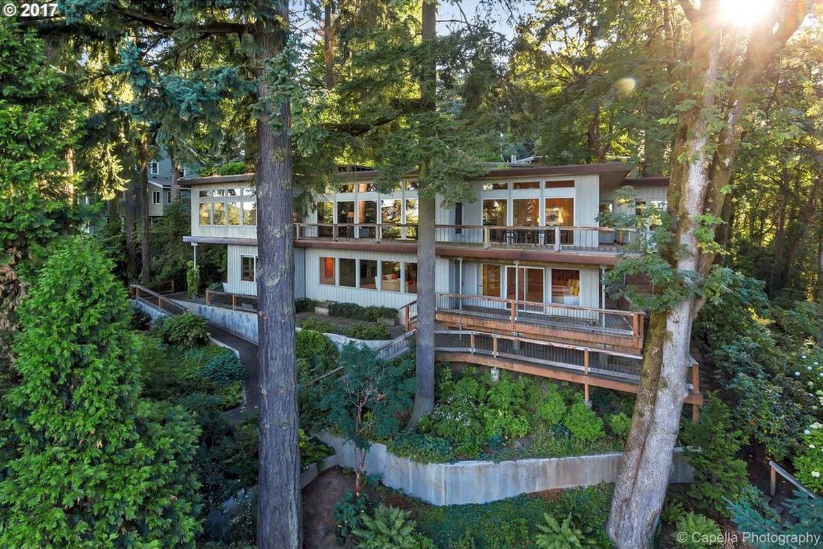 Multi-level modern home with sliding glass doors and wrap around balconies surrounded by trees. 