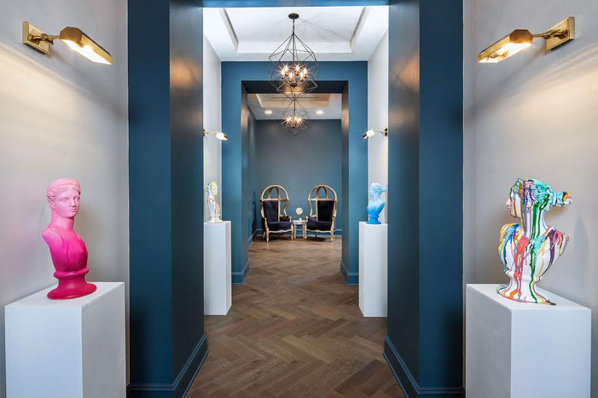 A long white and blue hallway at an apartment with wood floors and statues. 