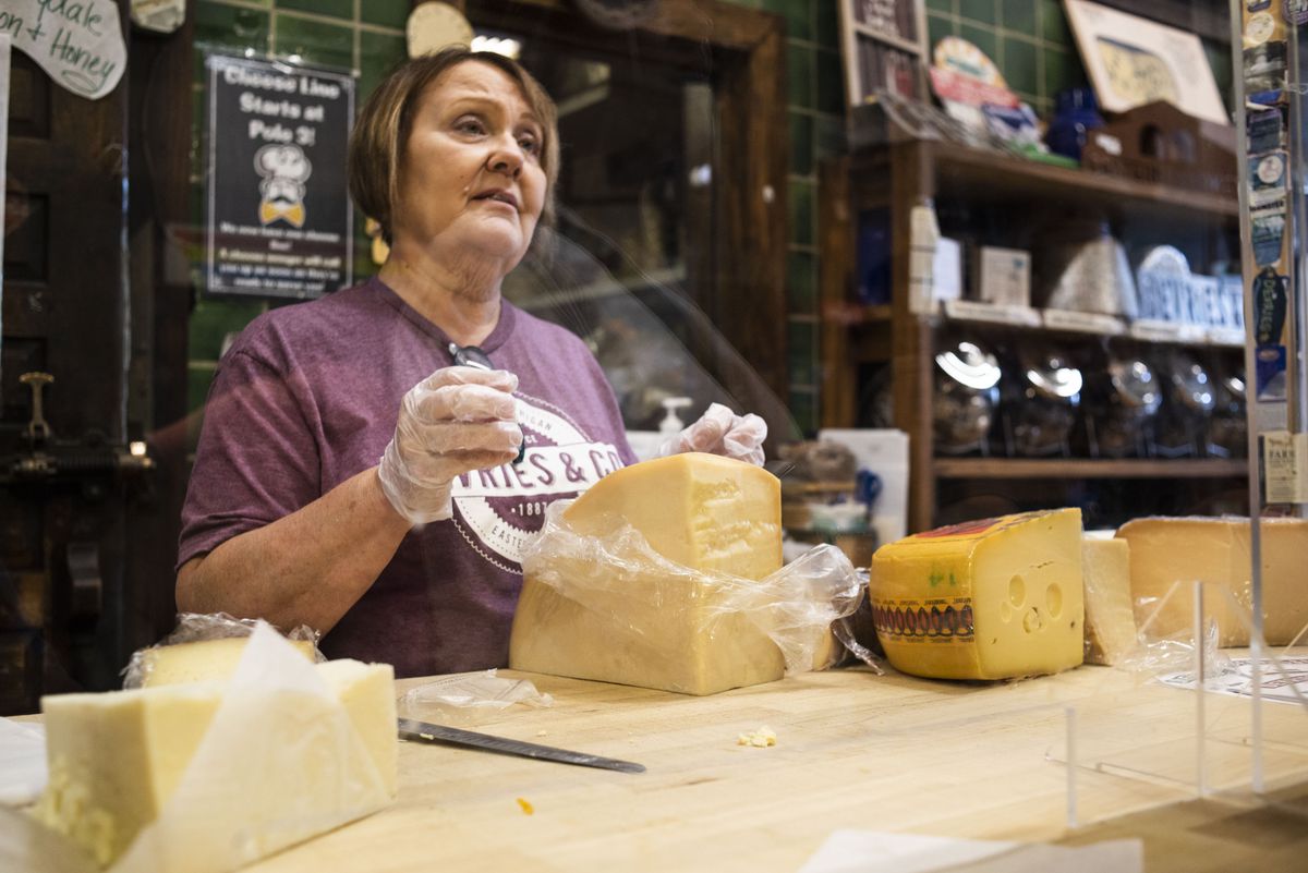 A woman with brown hair and a purple shirt standing behind some big pieces of cheese.