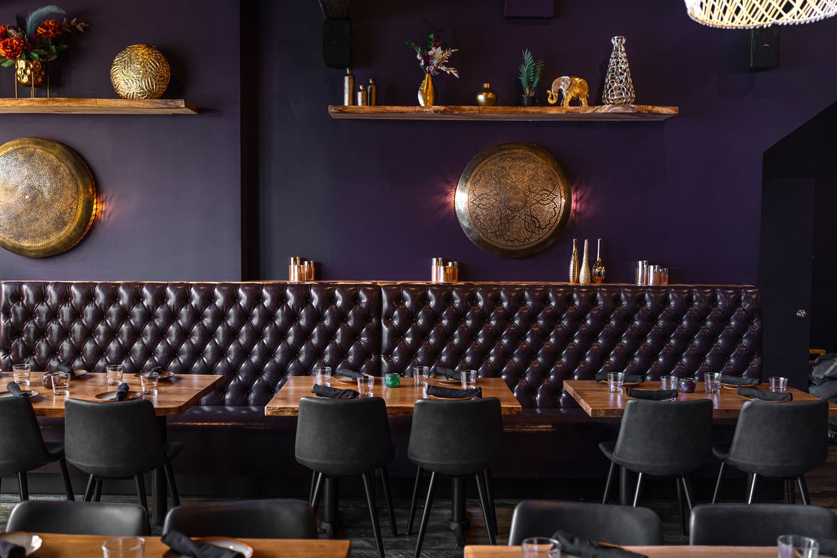 A dark upholstered leather banquette lined with four-top tables.