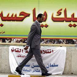 In this photo taken Feb. 16, 2010, Iraqi man walks past a campaign poster for Shiite Dawa Party reading in Arabic "Oh, Hussein, here we come to your aid," in Baghdad, Iraq.