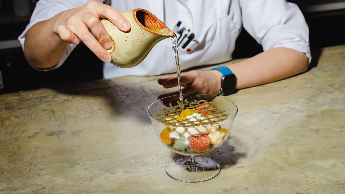 A person pours a pitcher into an elegantly arranged bowl of dessert