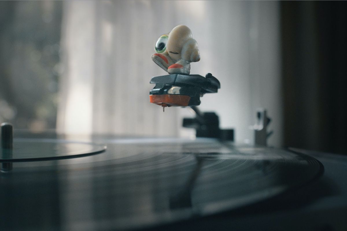 Marcel the Shell —&nbsp;a small seashell with googly eyes —&nbsp;stands on the raised arm of a record player in Marcel the Shell with Shoes On