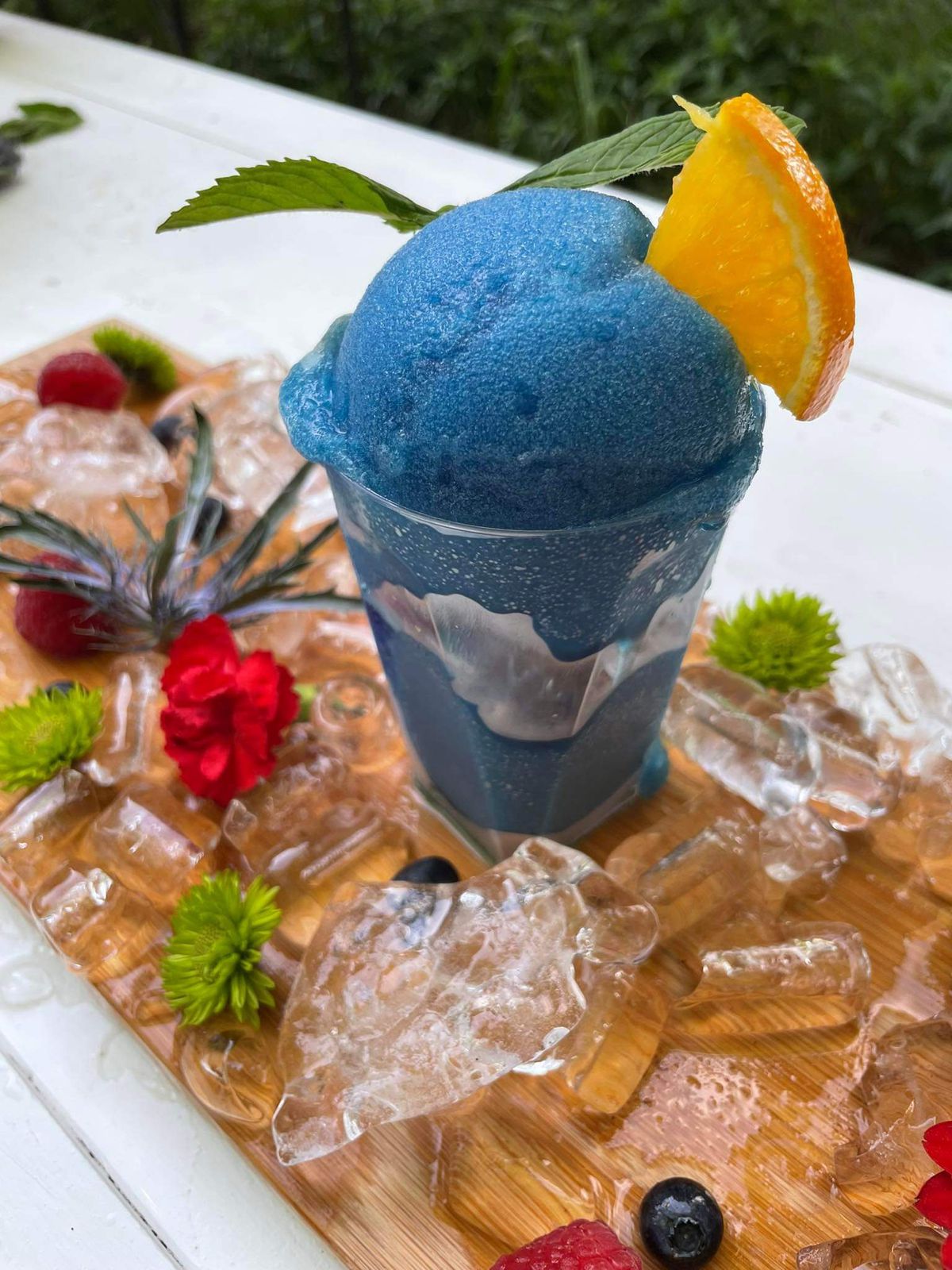 A blue slushy on a board surrounded with fresh fruit and flowers.