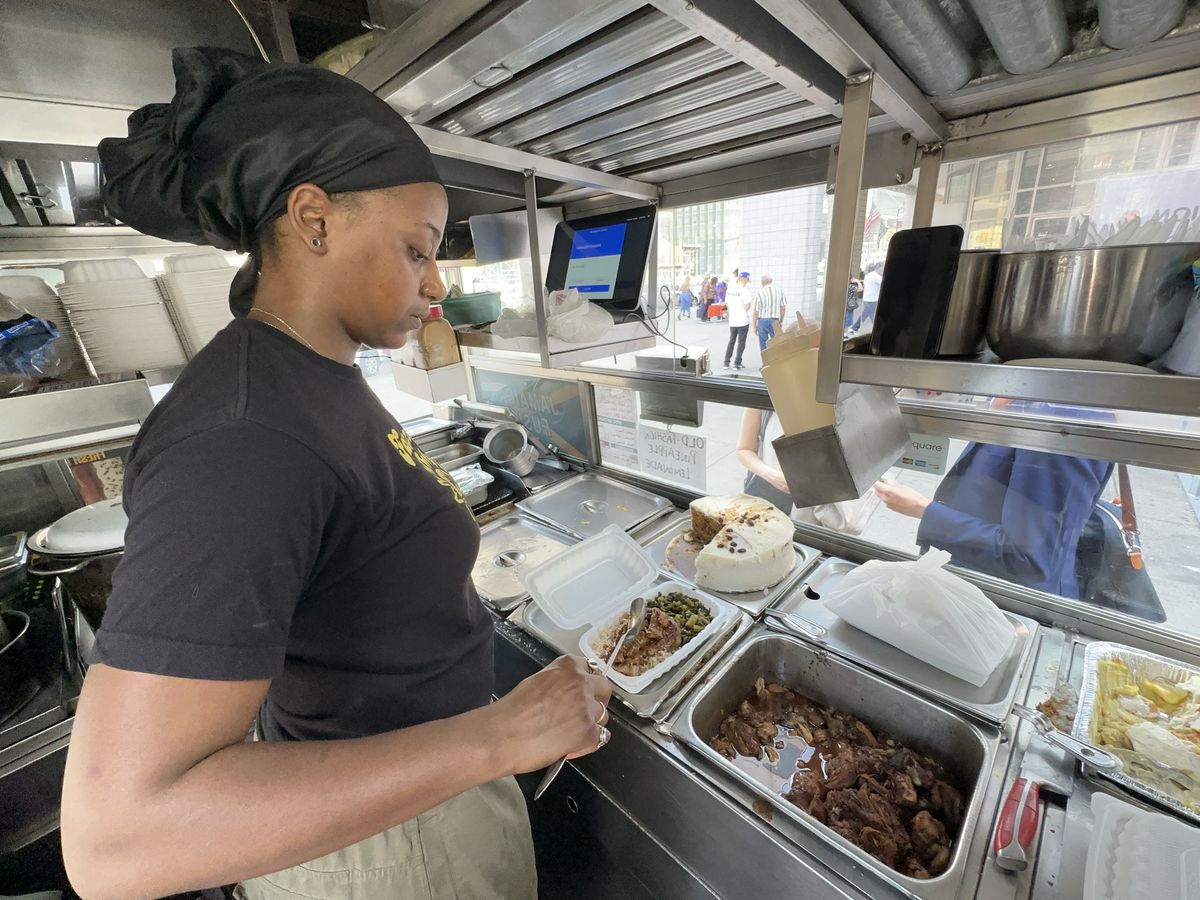 A woman preps another platter of their signature Jamaican cuisine inside a food truck.