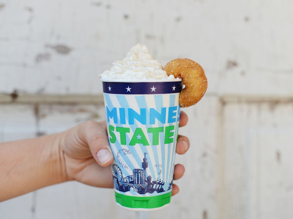 A Minnesota State Fair official cup topped with whipped cream and a mini doughnut hanging off the edge