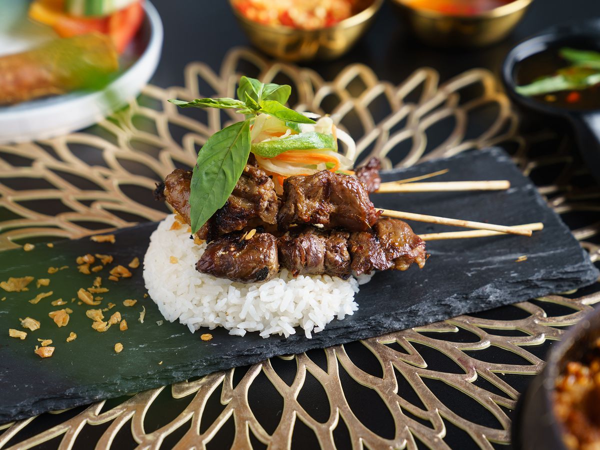 Skewers of cooked beef sit on a pile of white rice garnished with herbs and other vegetables.