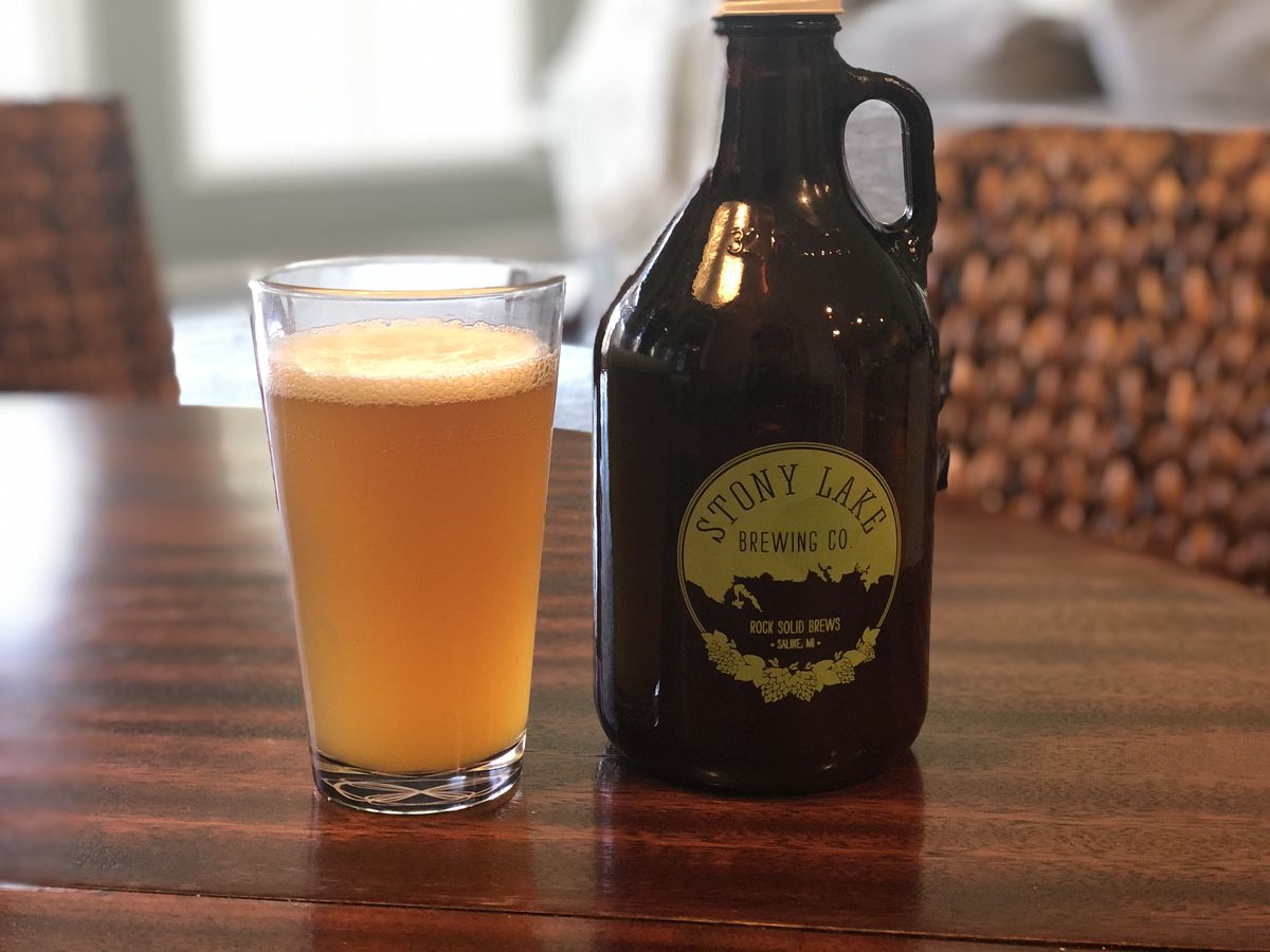 An amber beer in a pint glass next to a Stony Lake growler.
