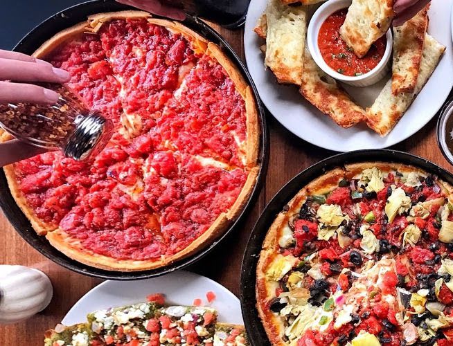 An overhead shot of deep dish pizza and other sides on a wooden table.