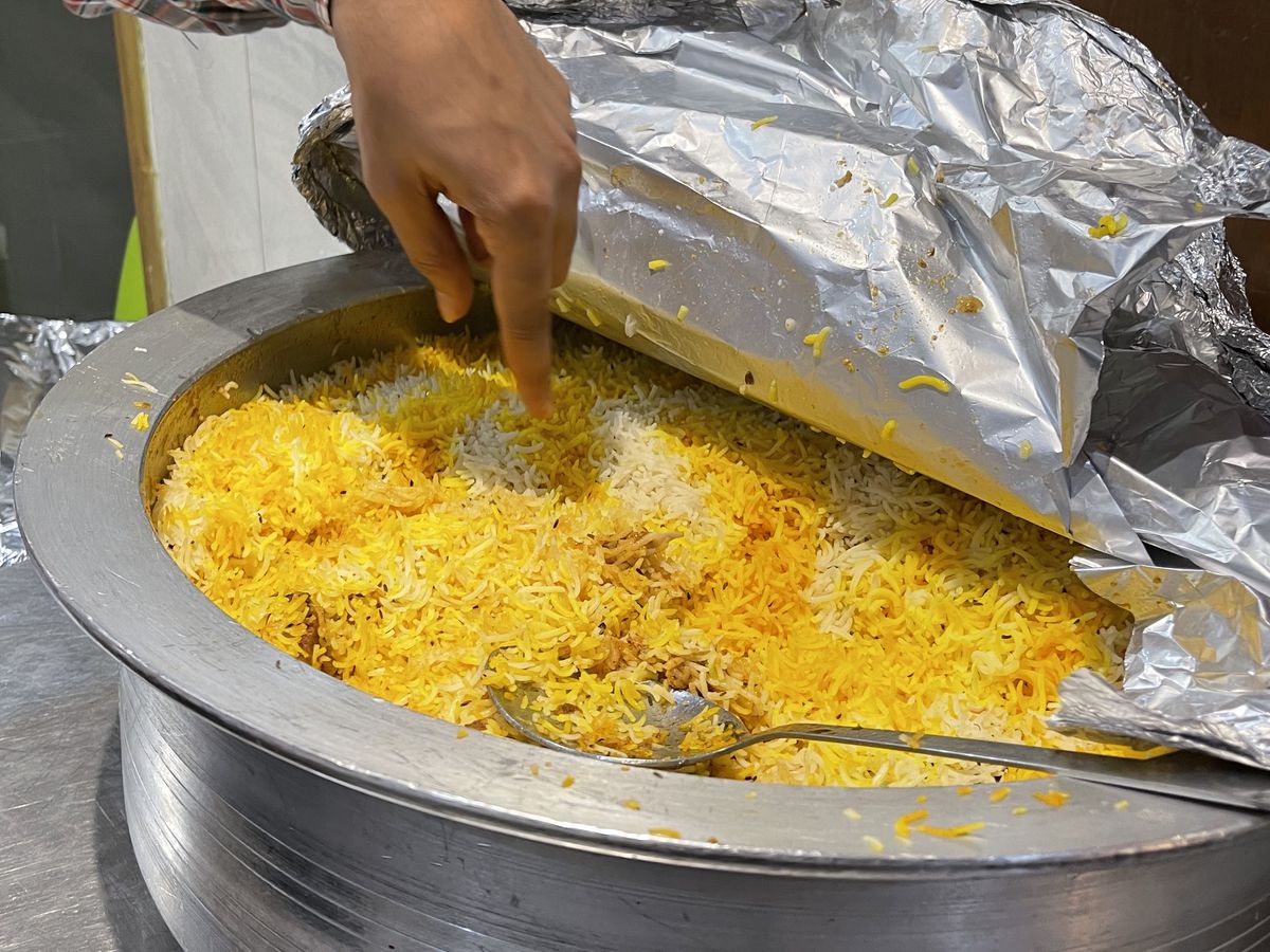 A pot of golden rice in a handi, a large aluminium cooking vessel, foil peeled back to reveal its cargo.