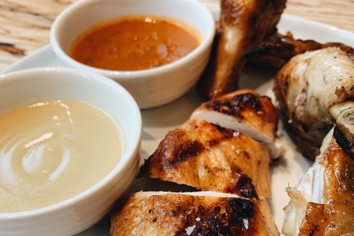 A picture of grilled chicken with sides of white and red sauces at Mama Bird