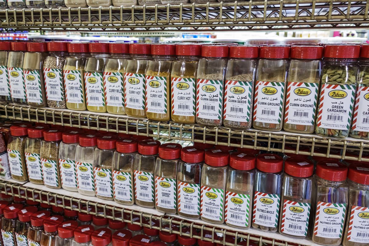 A slew of spices in plastic jars on grocery store shelves.