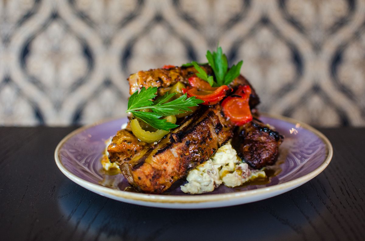 Thick baby back ribs are piled up atop a pyramid of potato salad and garnished with pickled cherry peppers. The plate sits on a black tabletop.