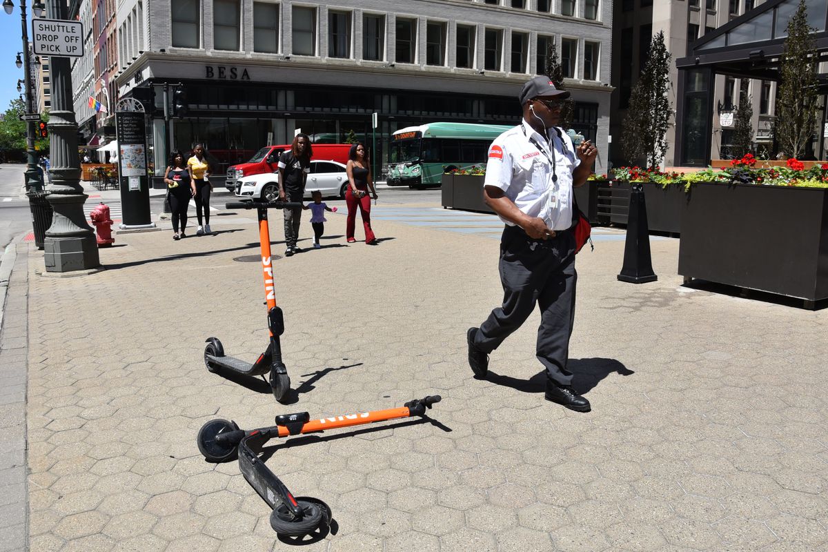 A security guard walks by two orange scooters on a sidewalk in Detroit.