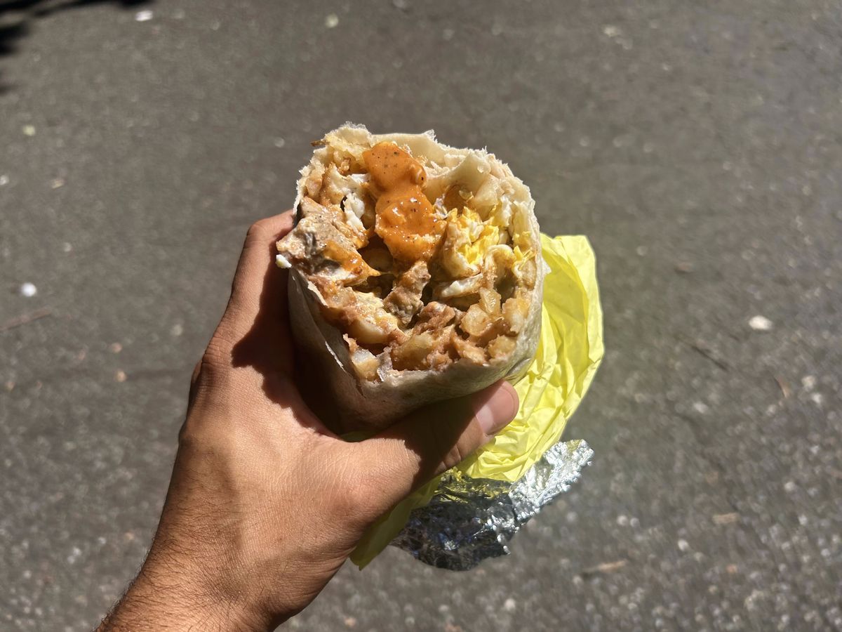 A hand holds up a burrito with bites taken out of it
