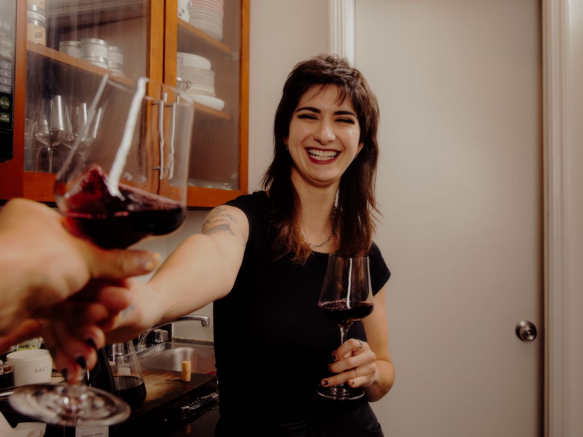 Camille Lindsley holds out a glass of wine toward the camera.