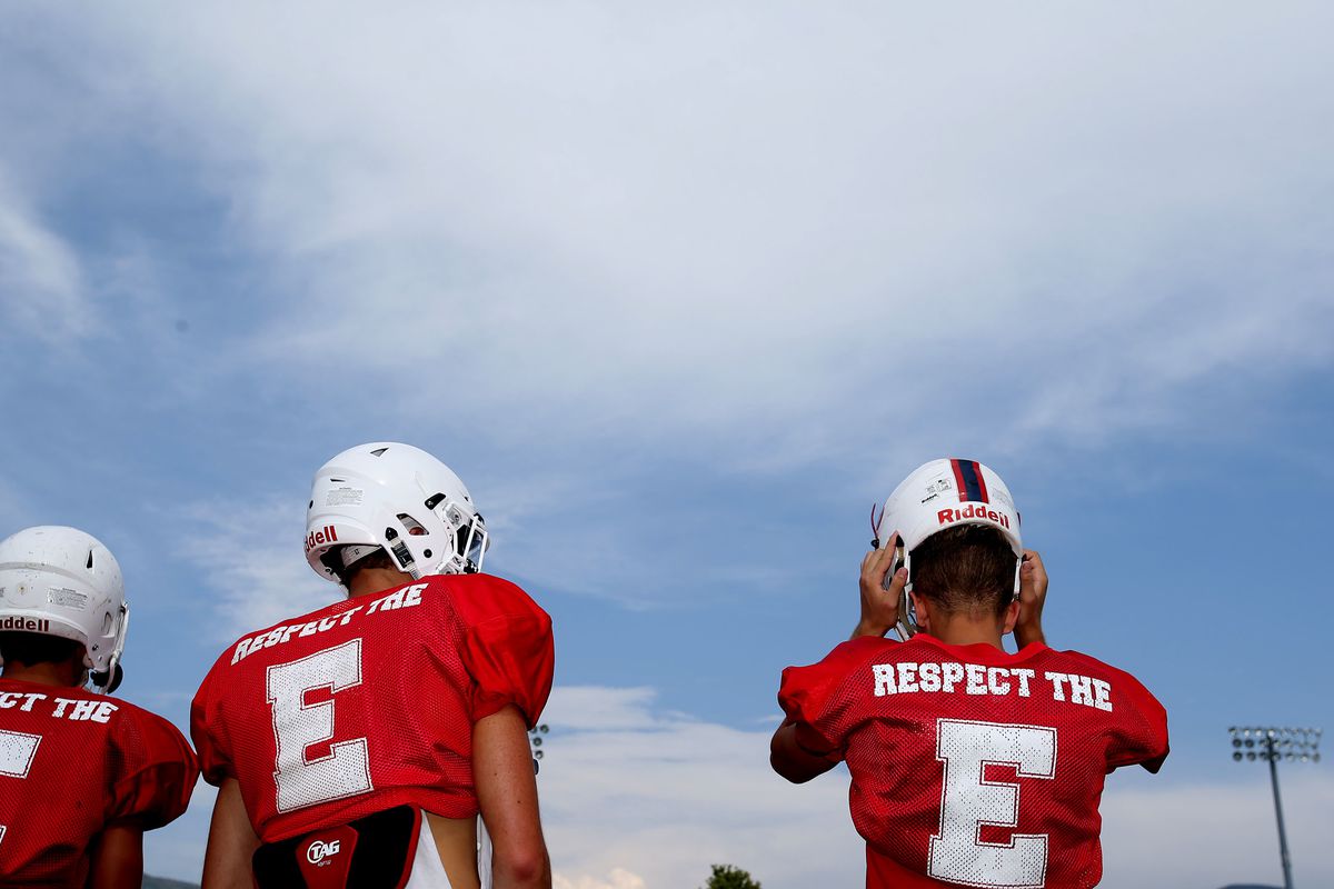 Football players put on their helmets during practice at East High School in Salt Lake City on Monday, Aug. 7, 2017.