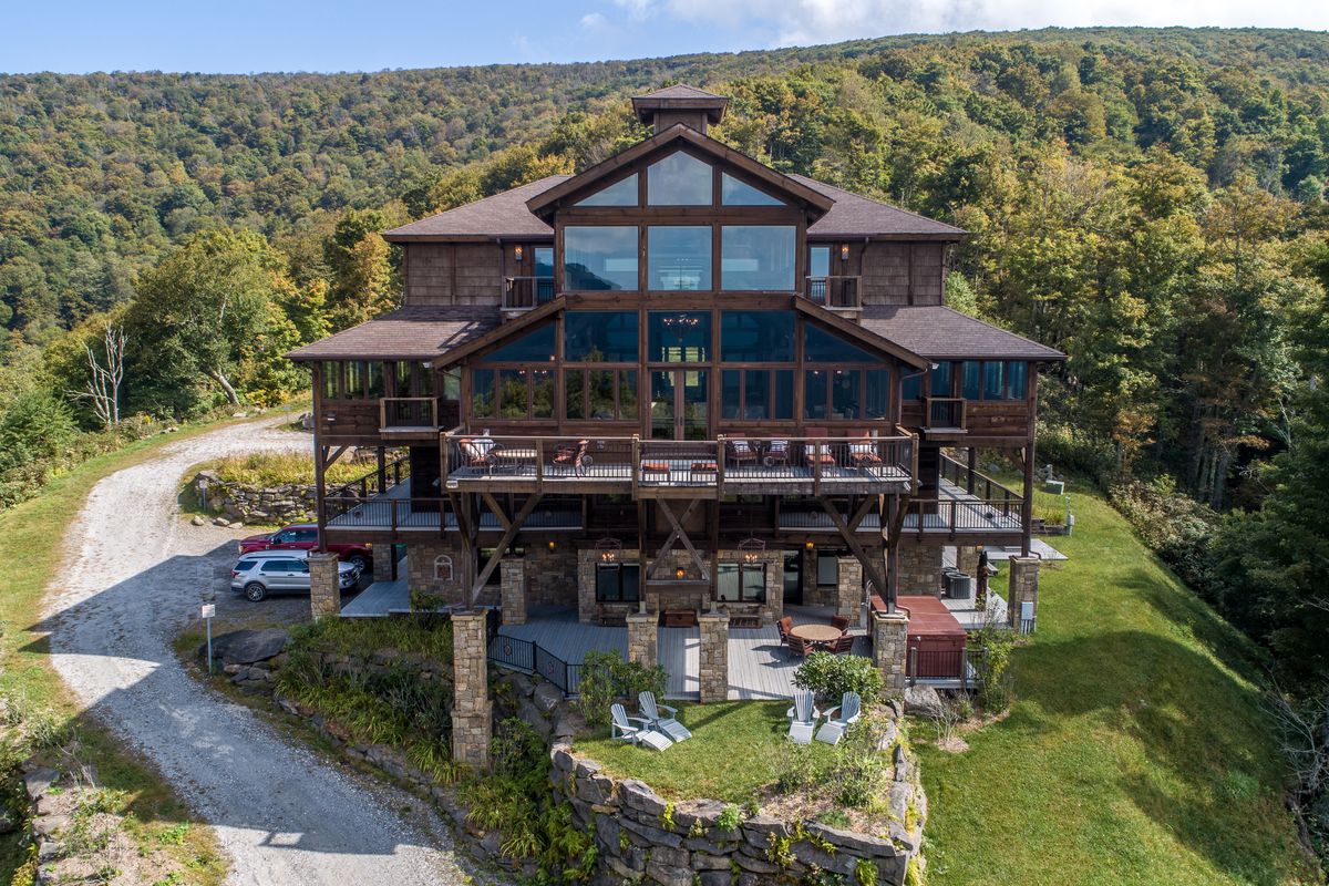 An aerial exterior view of a large timber home surrounded by mountains. 