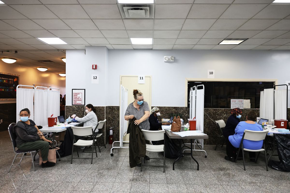 People receive COVID vaccines in an office space, with small white curtains separating recipients.