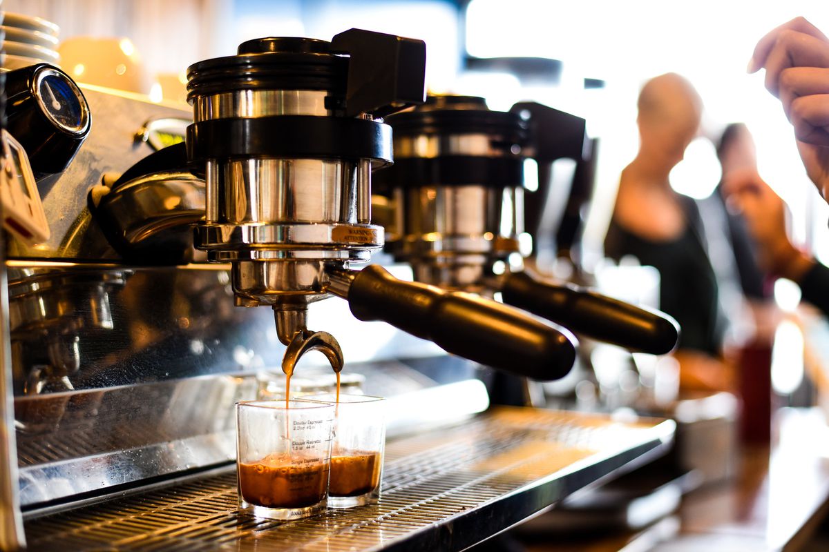 An espresso machine pulls light brown liquid into two small glasses.