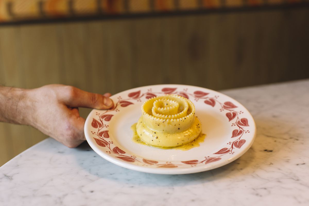 A plate with a single large noodle rolled into a spiral, dressed with olive oil and pepper