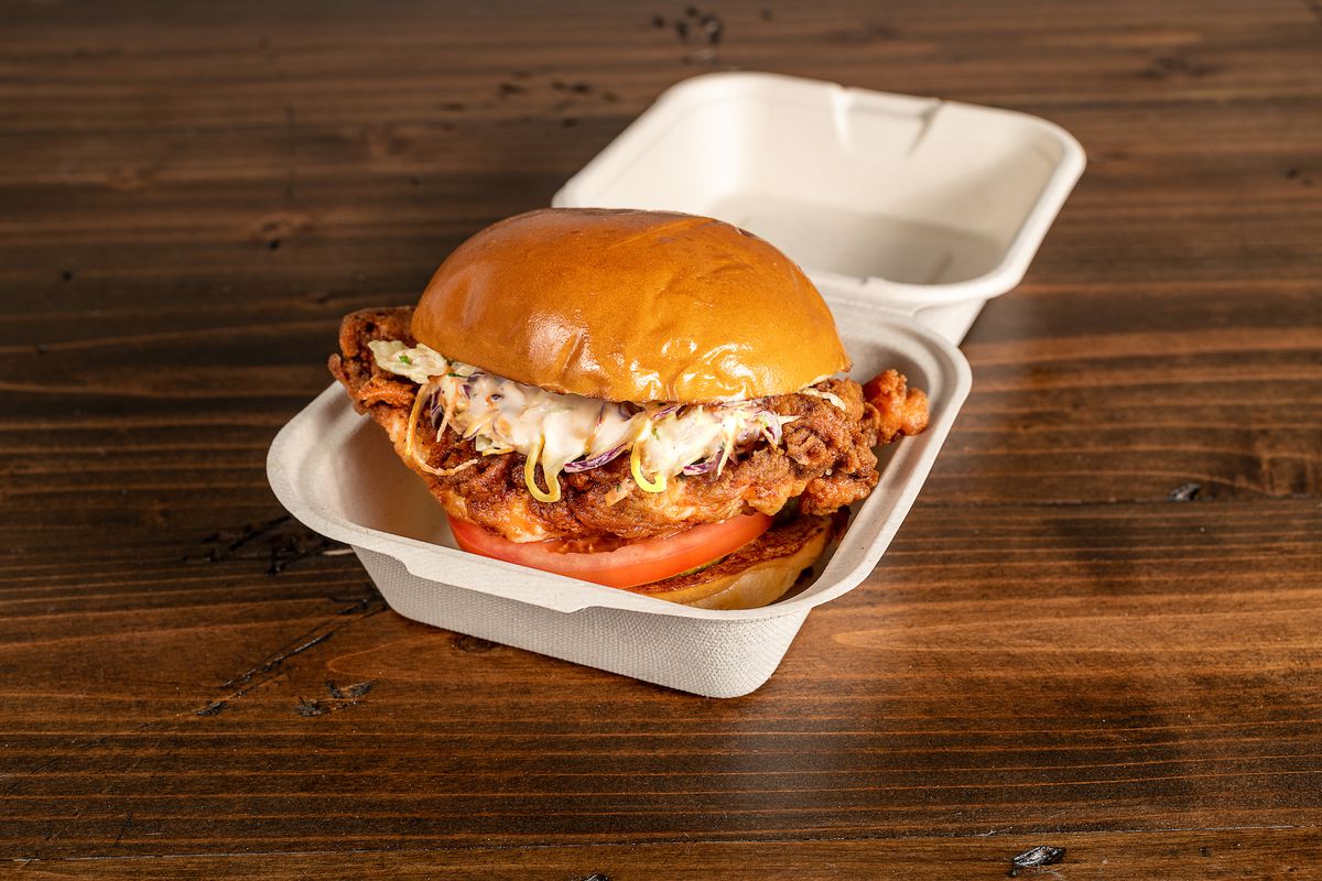 A close up shot of a clamshell takeout container holding a fried chicken sandwich with sauce.