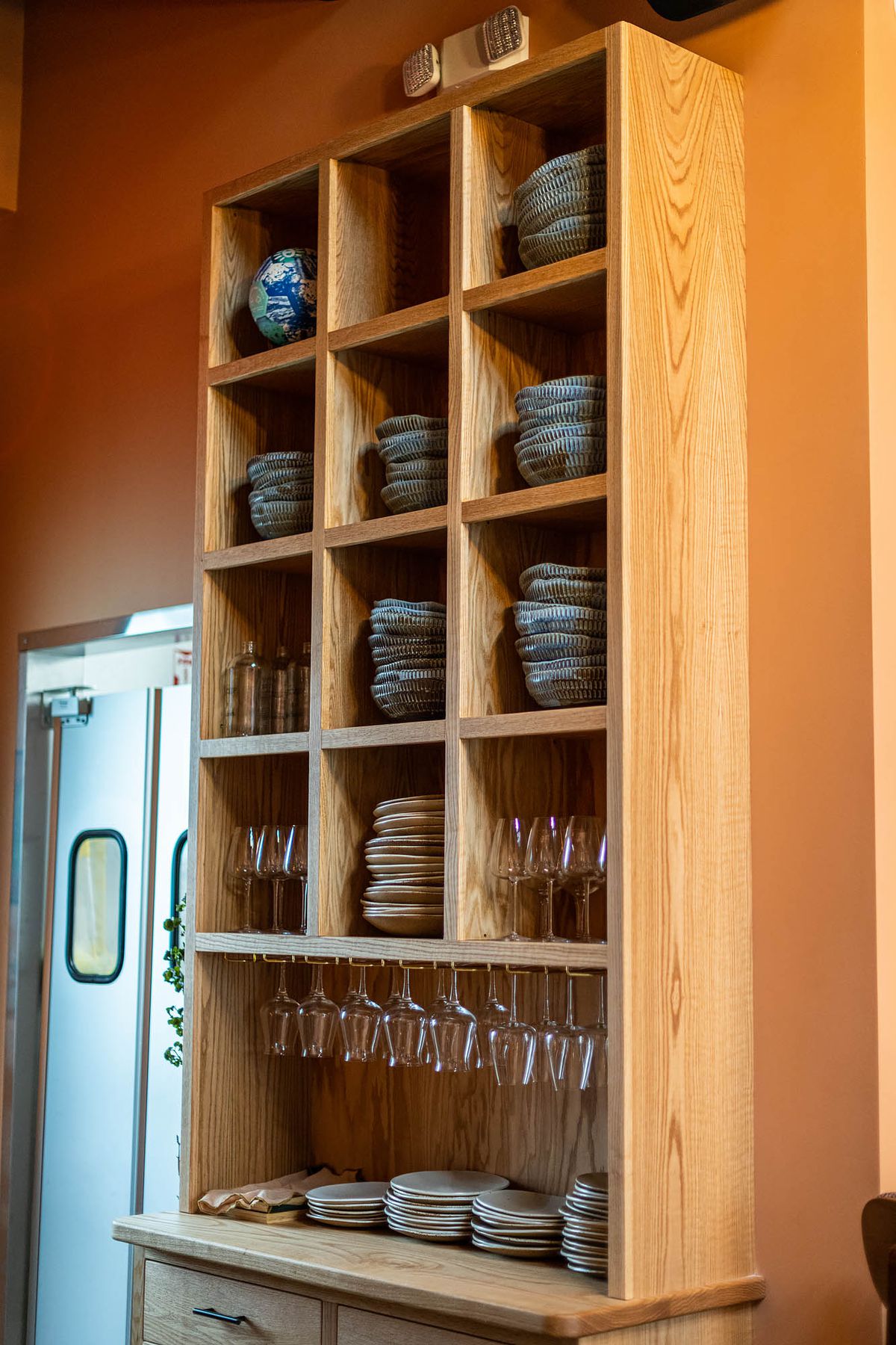 Bowls and plates stacked inside of wooden shelves at a restaurant.