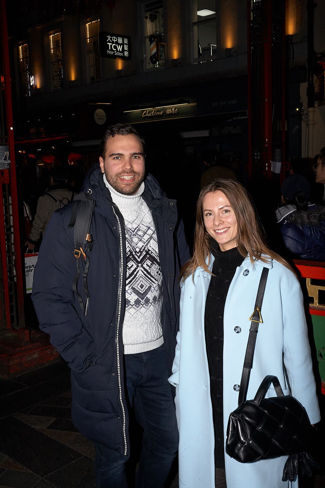 A man on the left wears a knit patterned turtleneck under an open parka while on the right a woman wears a light-blue coat.