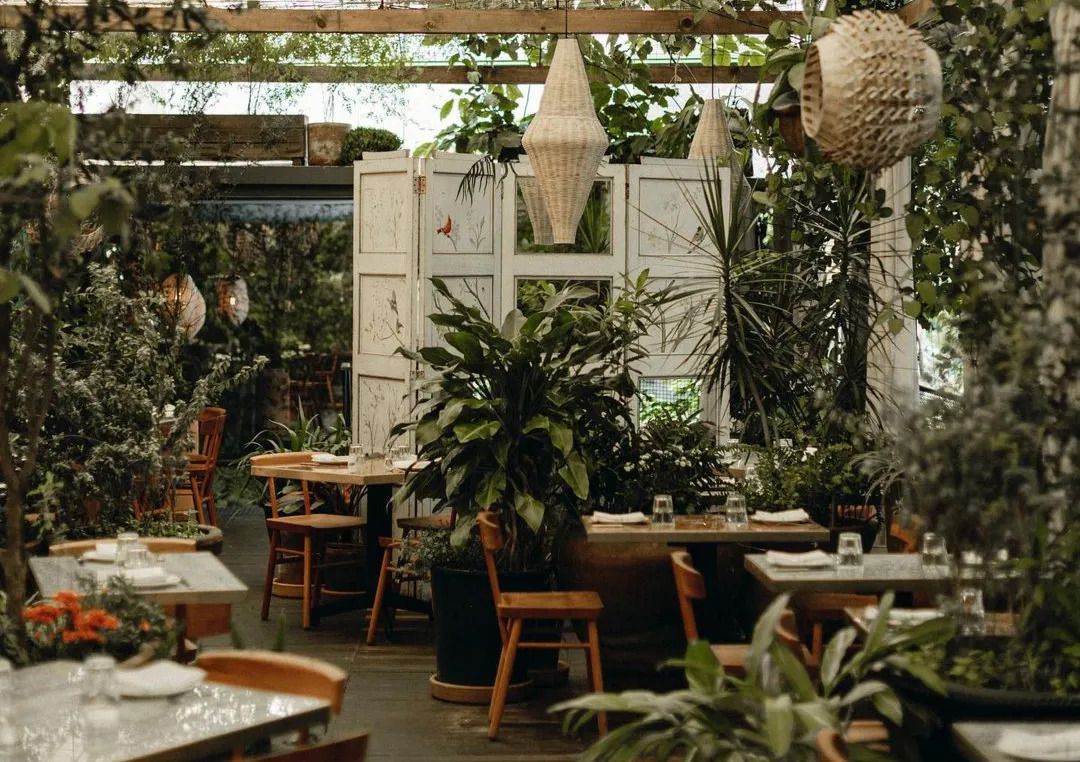 A covered outdoor seating space covered in greenery with hanging lanterns.