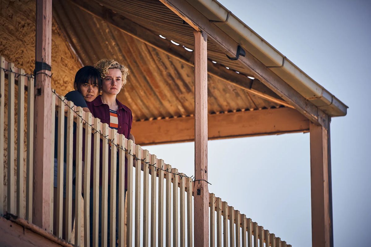 Two young woman stand on the balcony of a house.