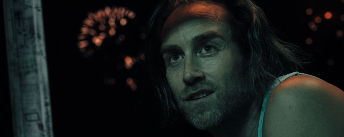 Levi (writer-director Justin Benson) stares offscreen in wide-eyed enthusiasm as fireworks go off in the distance behind him in a closeup from Something in the Dirt