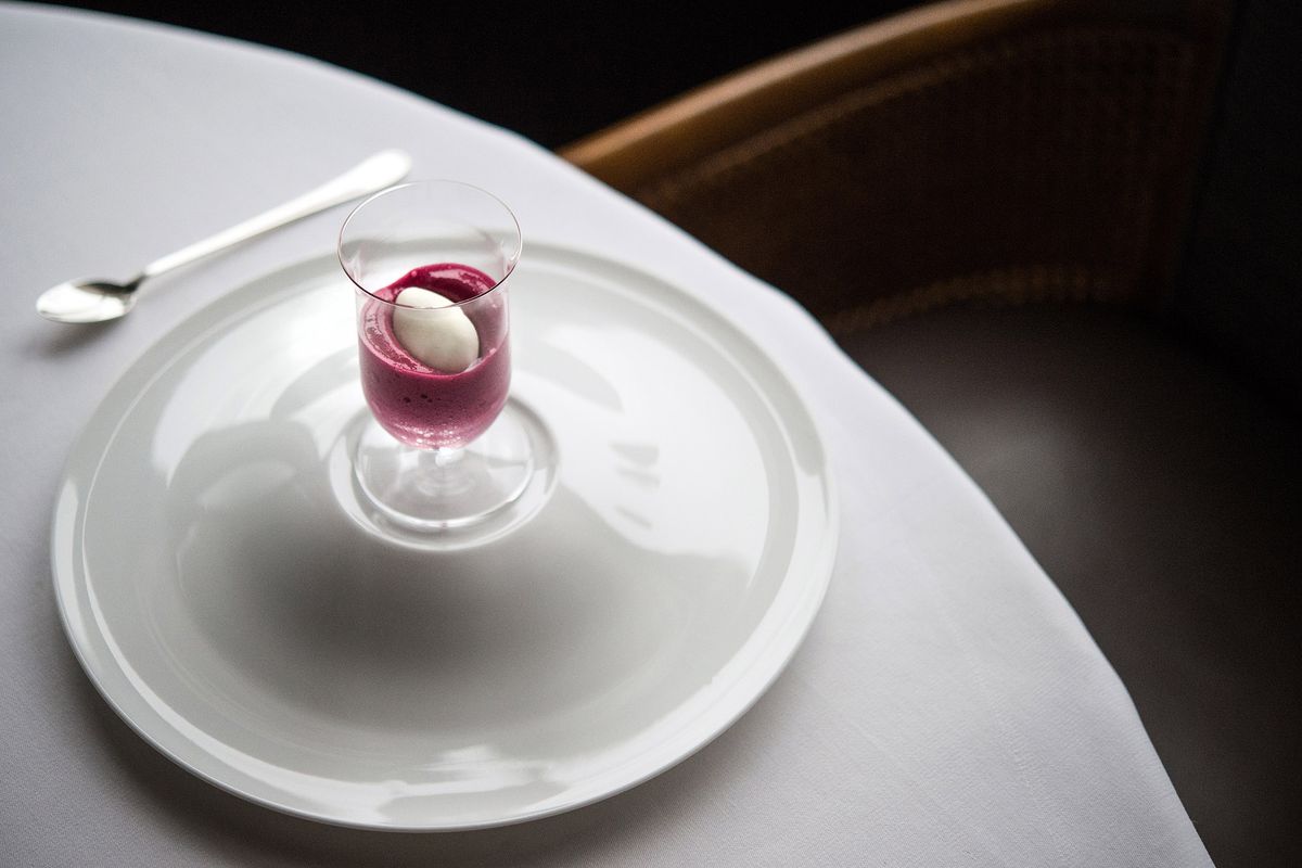 A purple-colored foam sits underneath a white quenelle in a clear glass on a white plate at Per Se