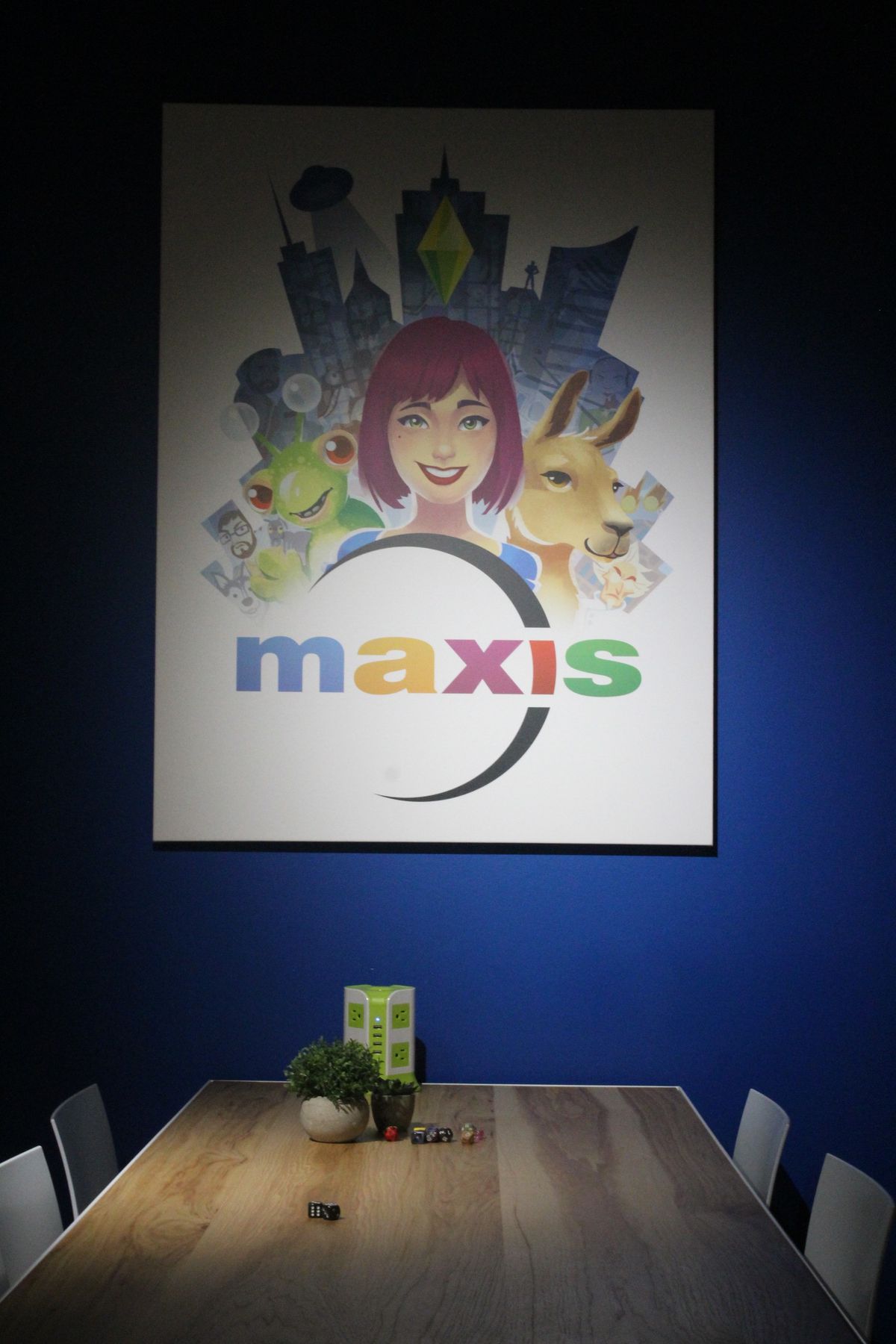 a Maxis poster hanging on a blue wall with a wooden table in front of it