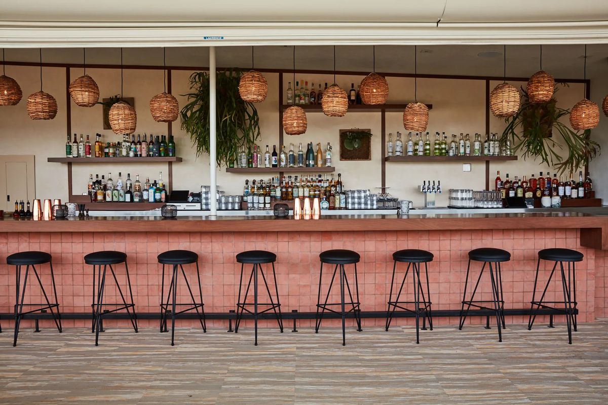 A pink bar with black wooden stools and hanging basket lights.