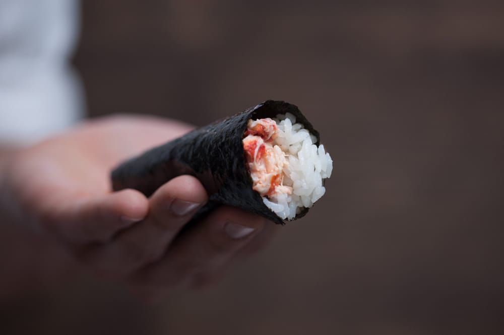 A hand shows off a hand roll of sushi.