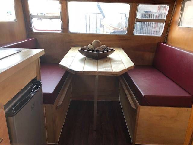 The interior of a camper trailer. There are dark red seats and a wooden table. 