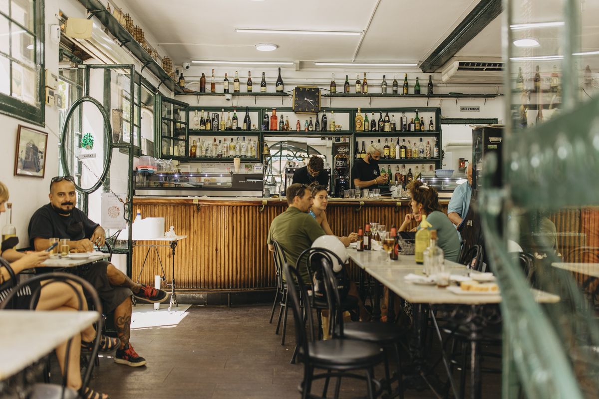 Tables of people in front of a wooden bar with bottles on the shelves.