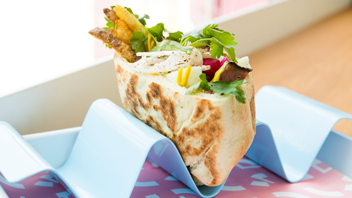a pita packed with smoked meat, vegetables, and herbs sits in a special holder that keeps it standing upright
