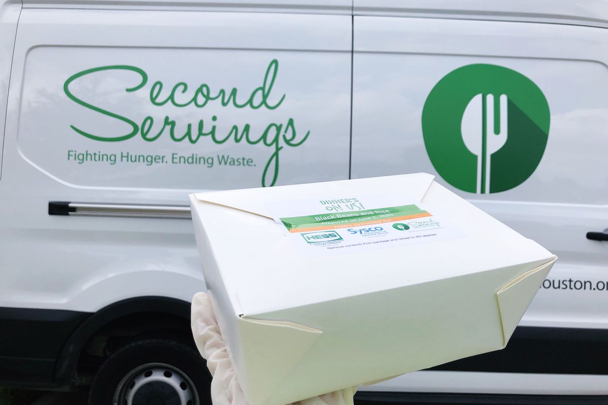 a gloved hand holding a white take-out box. in the background is a white van with the words “second servingsL fighting hugner, ending waste” on its side.