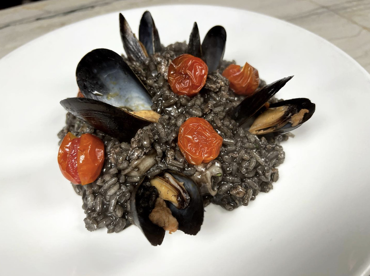 A seafood dish that includes risotto, mussels, and stewed tomatoes. 