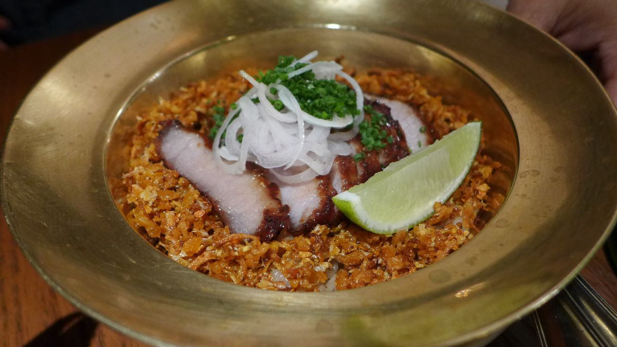 A golden bowl with a wide brim with orange rice and pale slices of meat.