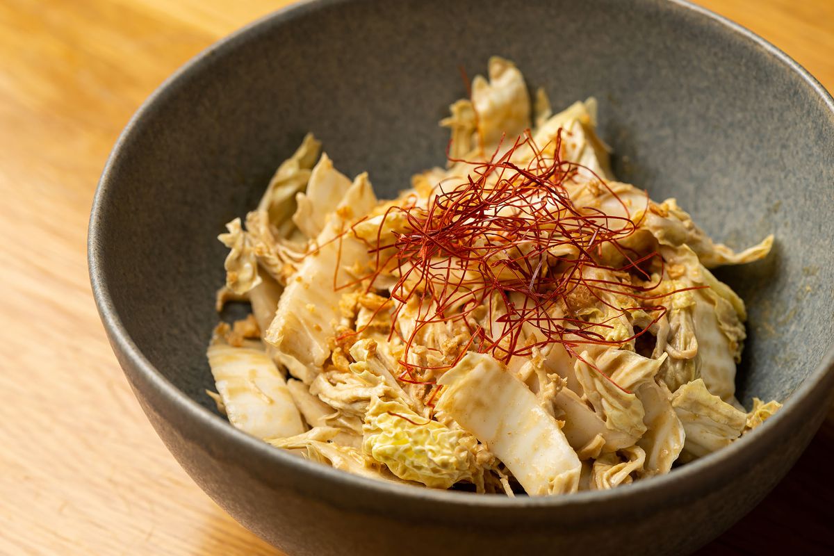 A gray bowl with slices of yellow cabbage and red chile threads.