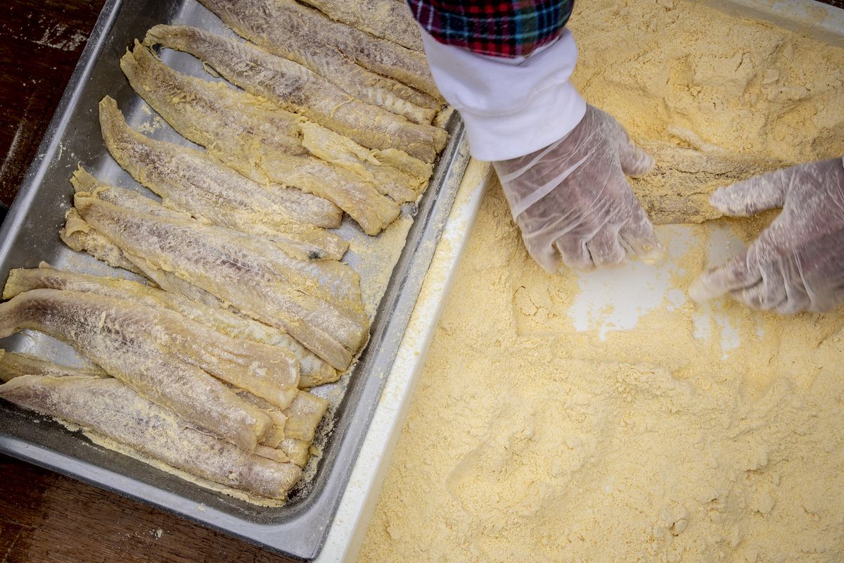 A pair of hands moving through flour next to fish filets.
