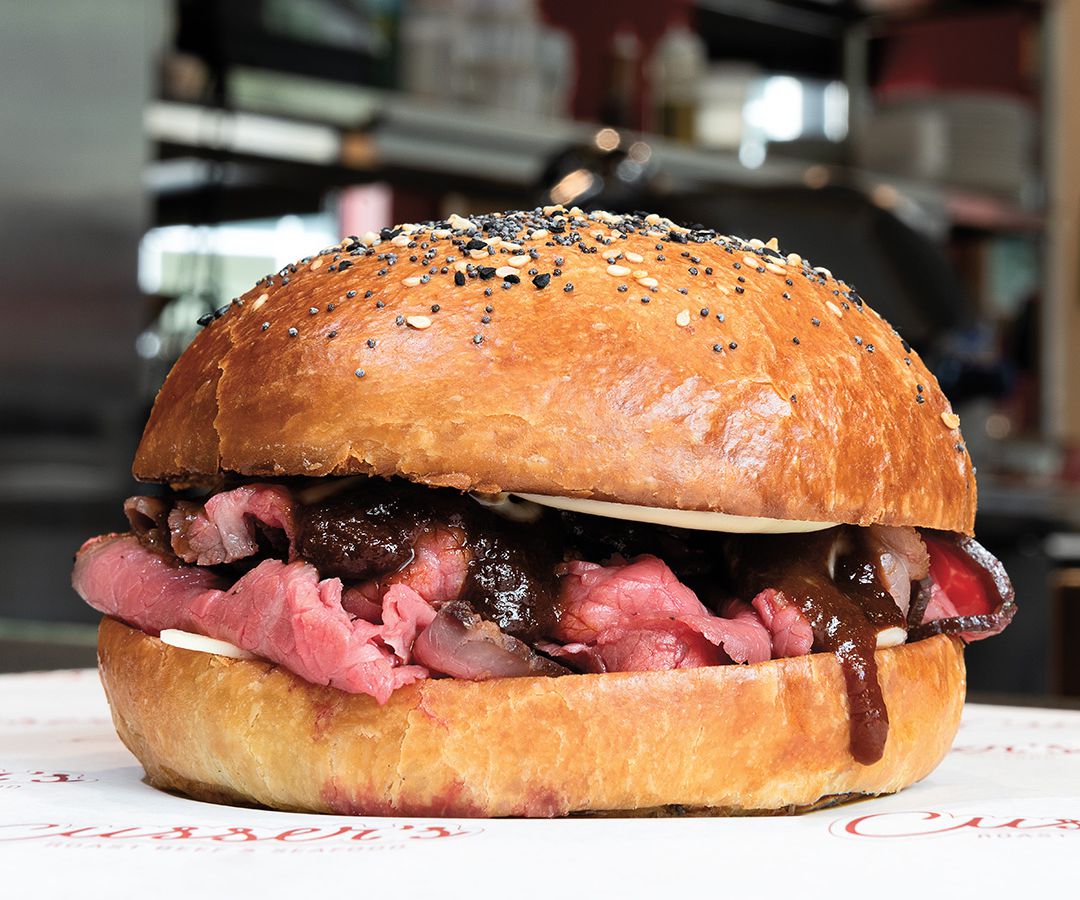 A roast beef sandwich with rare beef and barbecue sauce. The bun has sesame seeds and poppyseeds on top.