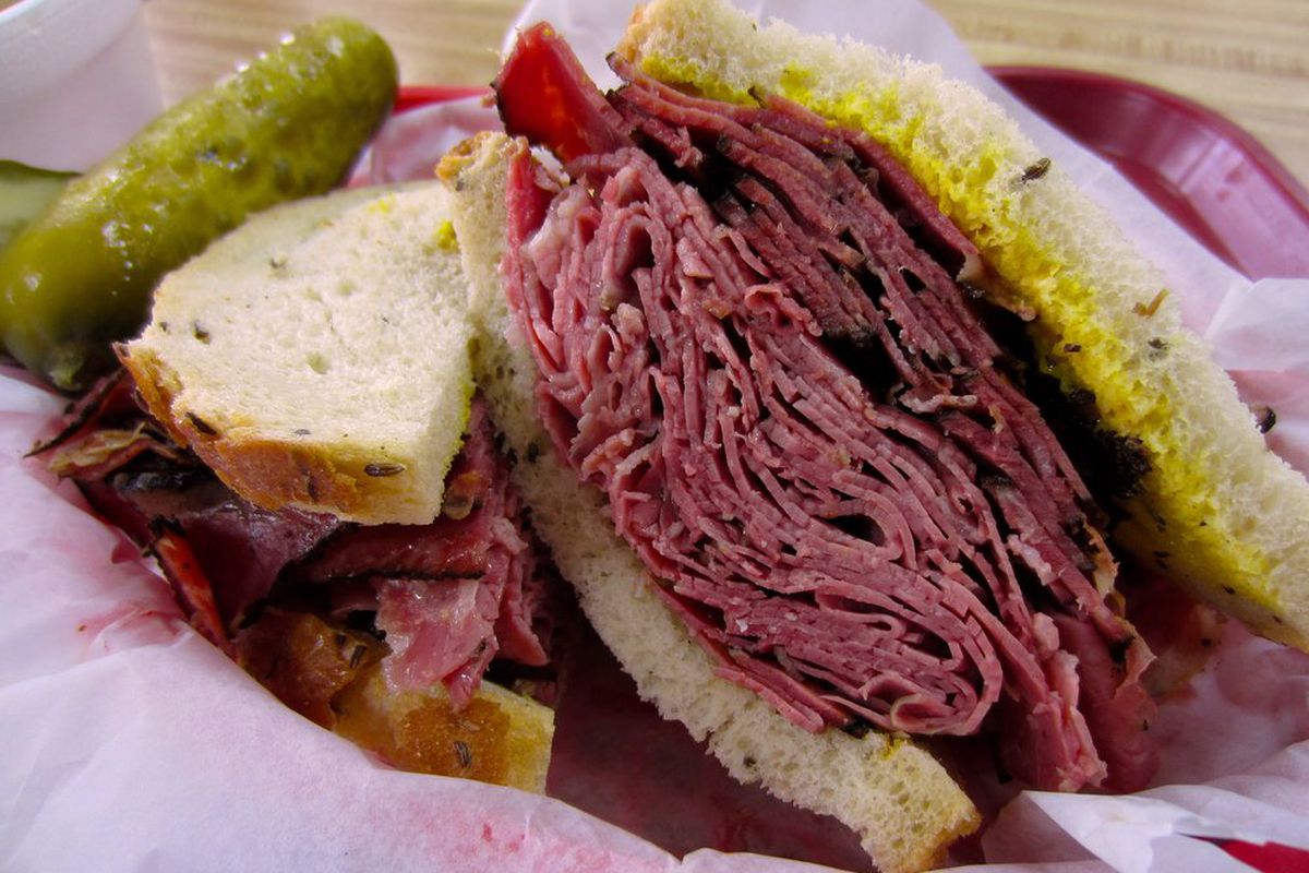 A stack of pastrami inside a sandwich with lots of mustard.