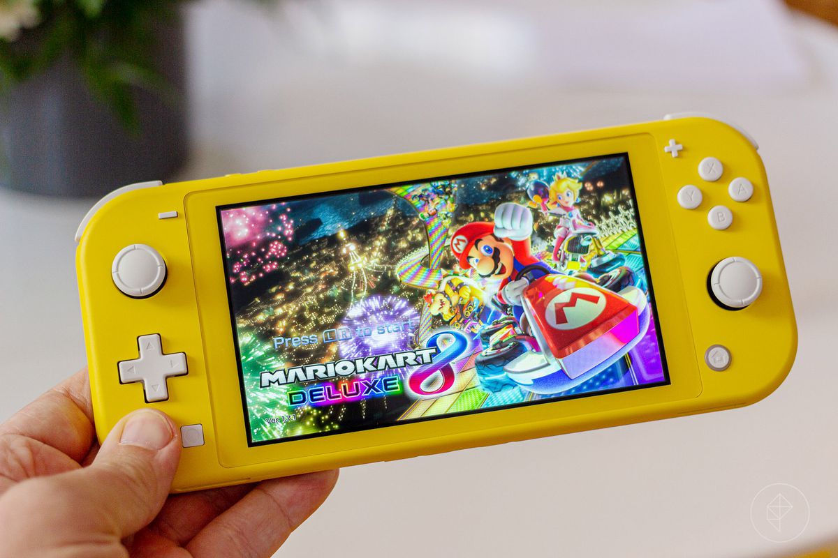 a hand holding a yellow Nintendo Switch Lite showing Mario Kart 8’s title screen