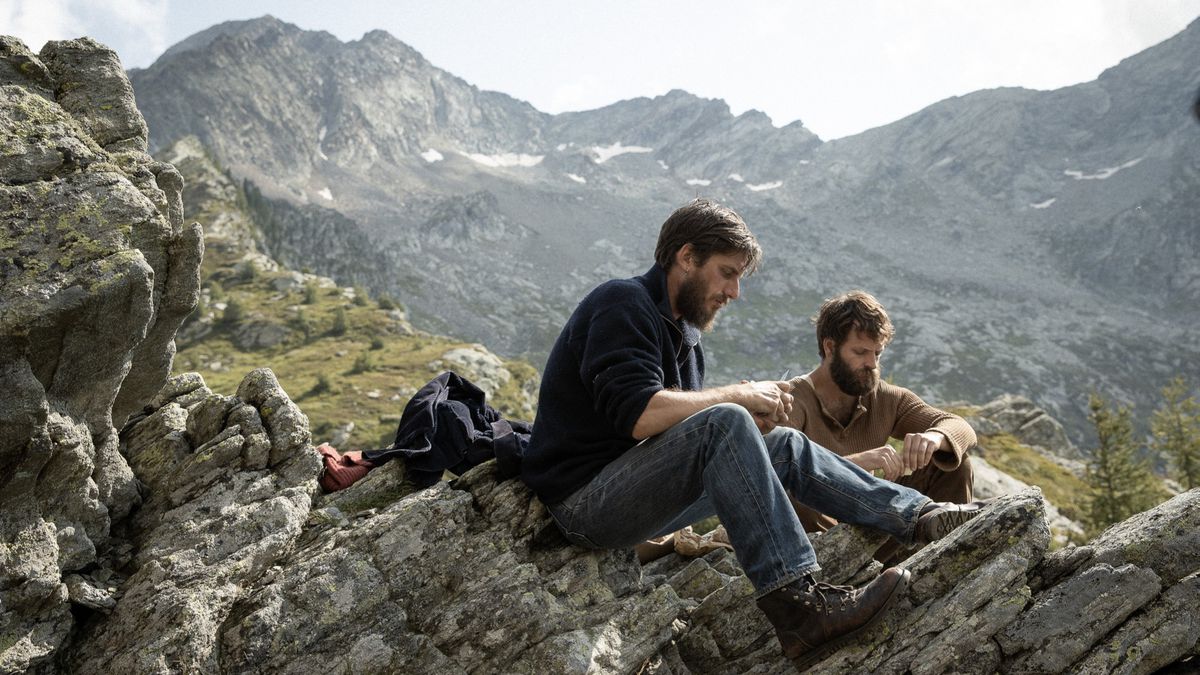 (L-R) Luca Marinelli and Alessandro Borghi sitting on a mountain overlooking another larger mountain range in The Eight Mountains.