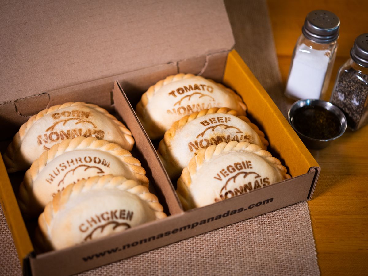 A box of butter-flecked empanadas with stamps indicating the fillings, on a wooden table.