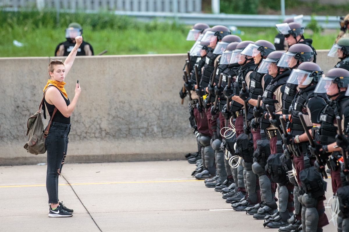A woman stands in front of a line of Minnesota police.