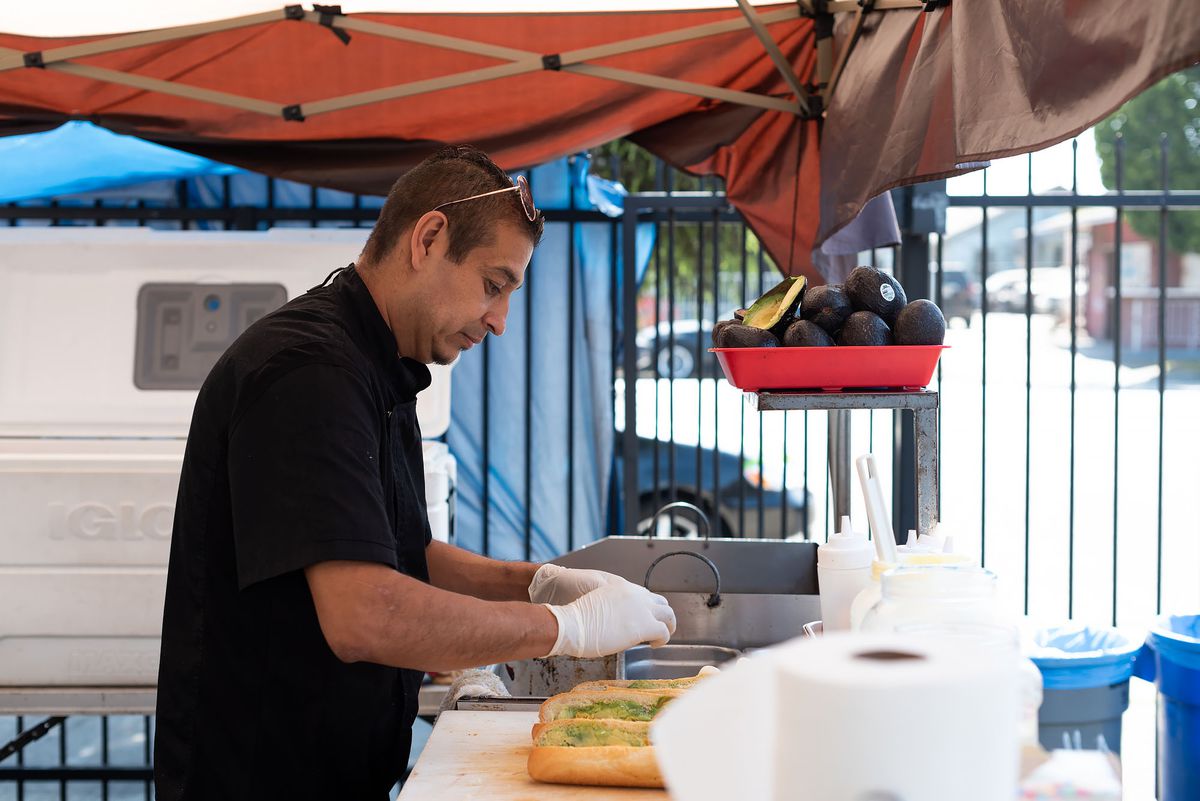A street food chef prepares sandwiches under a tent.